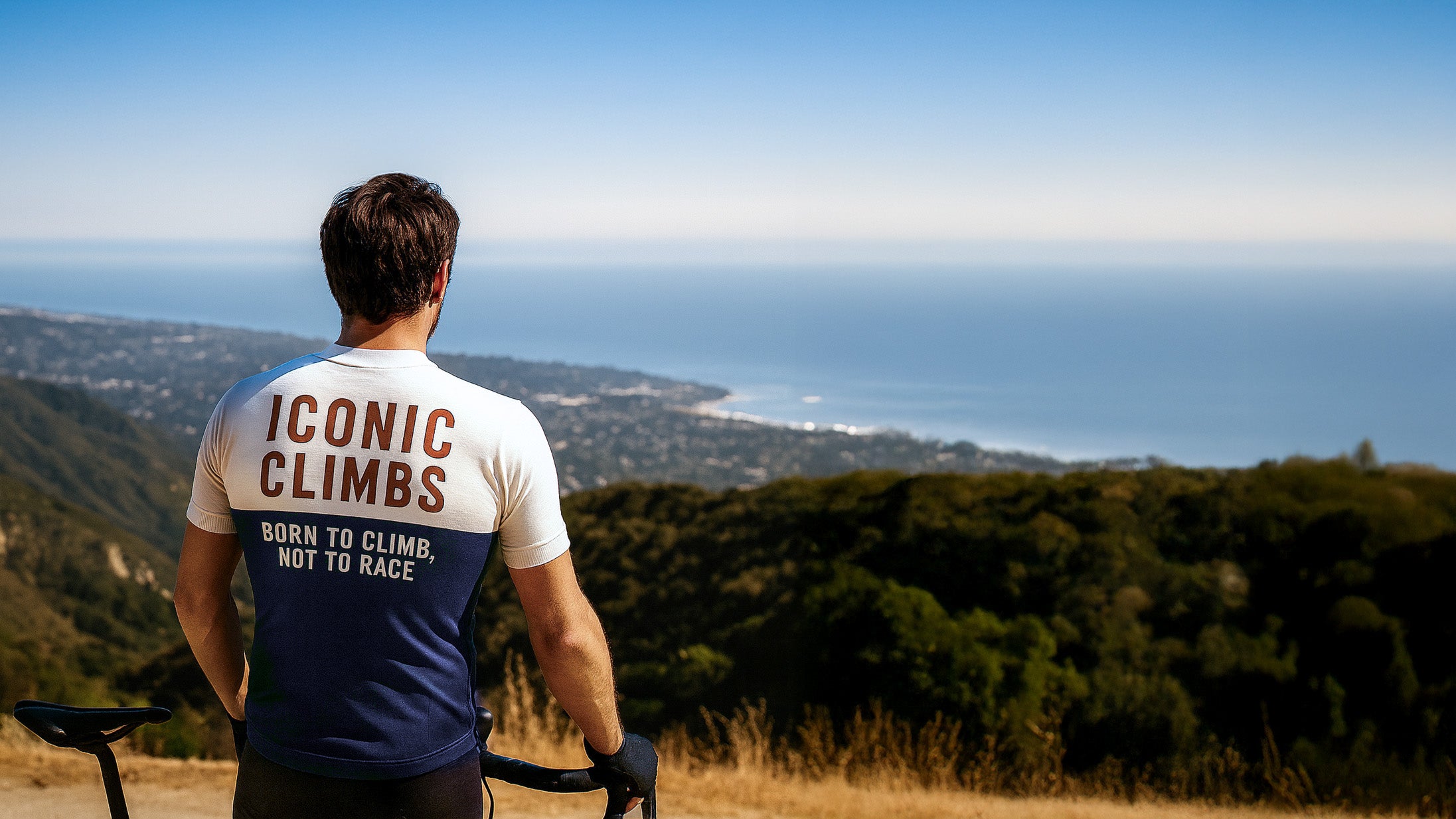 Person wearing an 'Iconic Climbs' shirt overlooking a scenic landscape with mountains and ocean.