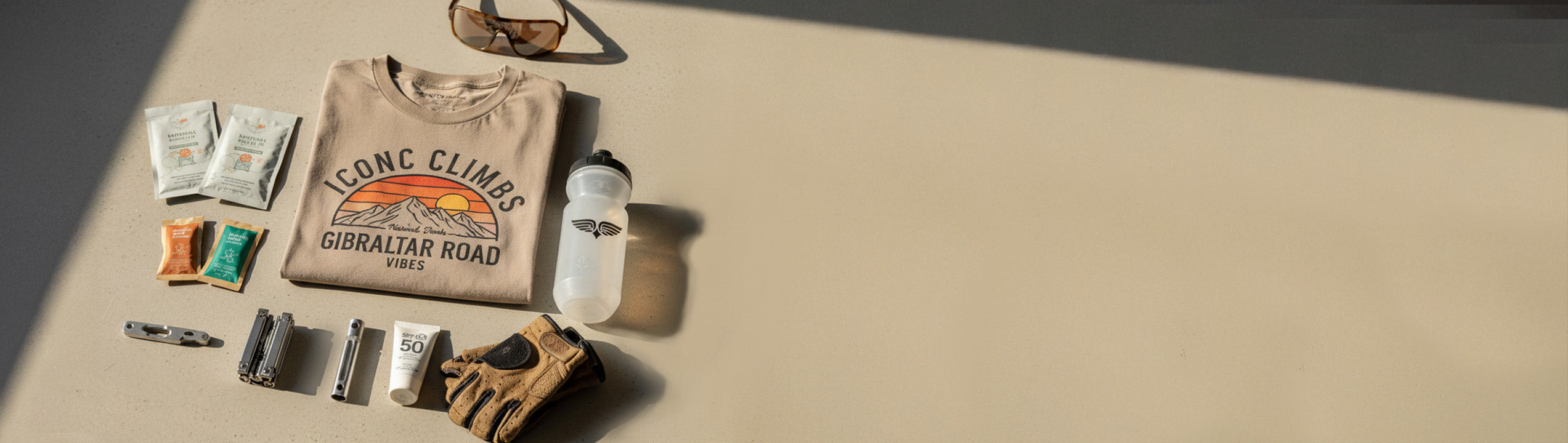 Collection of outdoor gear including a sweatshirt, sunglasses, and gloves on a beige surface.